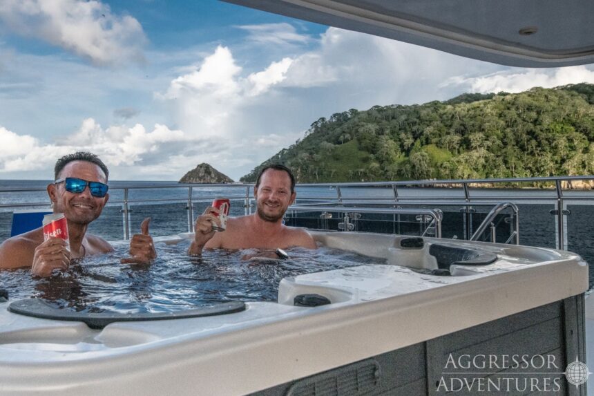 Two divers relaxing with drinks in the shaded hot tub on deck