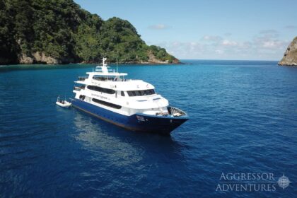 Cocos Island Aggressor liveaboard anchored in deep blue water beside a steep forested island