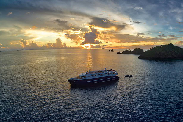 Aerial sunset view of the Blue Manta anchored near limestone islands in Raja Ampat