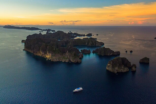 Aerial view of Raja Ampat's karst islands at sunset with the Blue Manta below