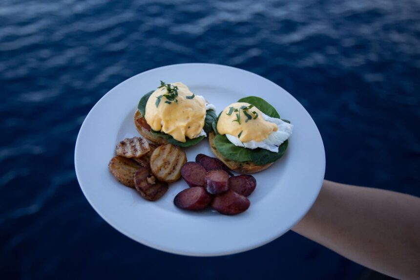 Plate of eggs benedict with grilled potatoes held over the ocean