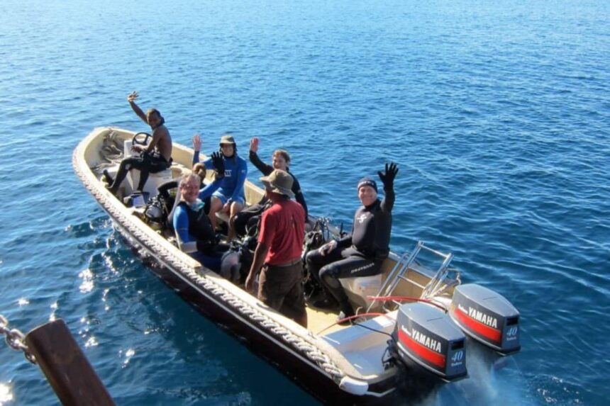 Divers waving from a small boat heading out to a dive site aboard the Arenui
