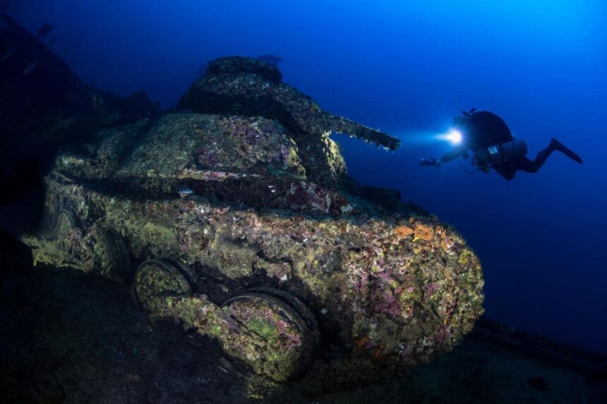 Diver shining a light on a moss-covered tank wreck in Truk Lagoon