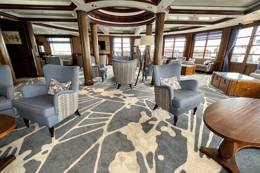 Wood-paneled lounge on the Caledonian Sky with armchairs and patterned carpet