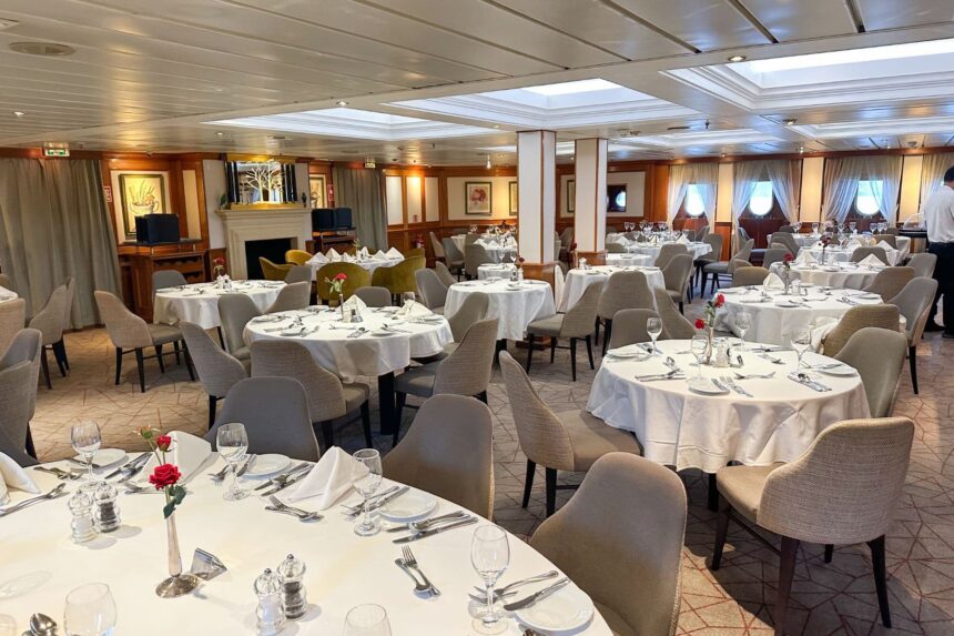 Formal dining room on the Caledonian Sky set with white tablecloths and roses