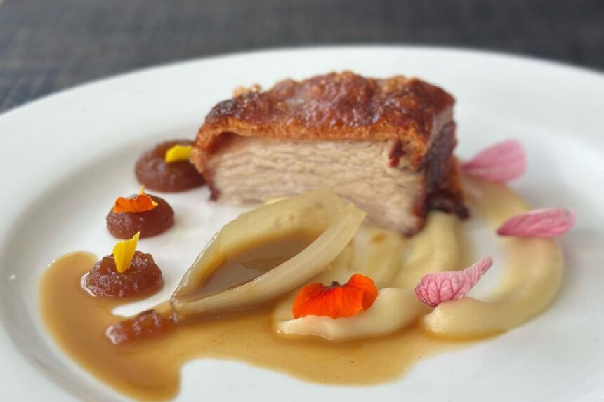 Plated pork belly dish with fruit puree and edible flowers