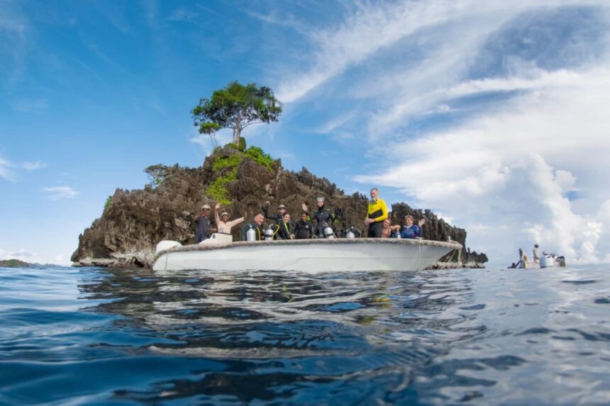 Divers wave from a small dive tender near a rocky jungle-topped islet