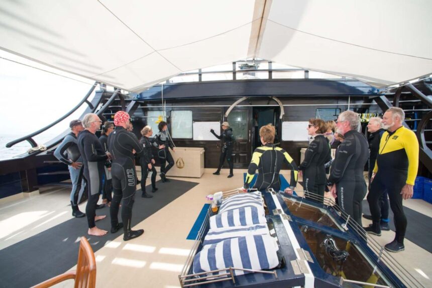 Divers in wetsuits gather on deck for a dive briefing aboard the Dewi Nusantara