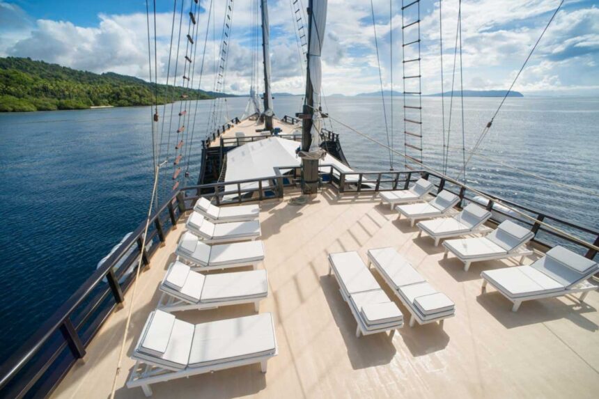 Rows of white sun loungers on the wooden deck of the Dewi Nusantara under sail
