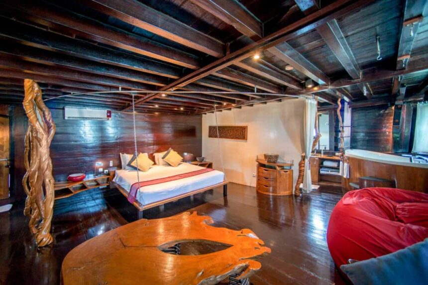 Wood-paneled cabin on the Dewi Nusantara with a hanging bed swing and carved wooden decor