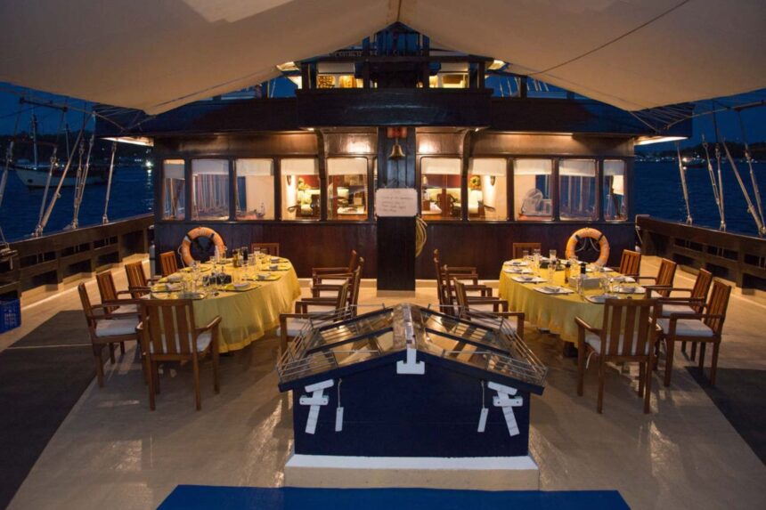 Dinner tables set with yellow linens on the Dewi Nusantara's deck at dusk