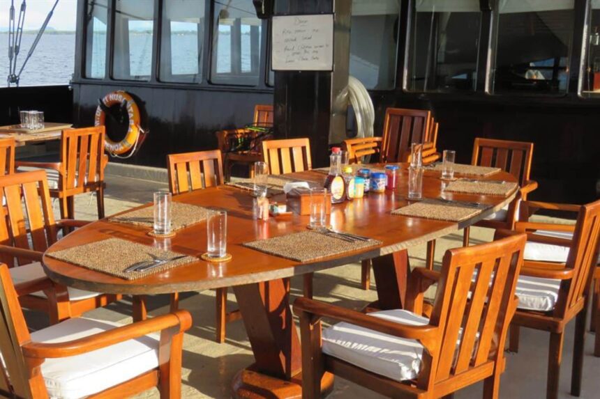Long dining table set for a meal on the Dewi Nusantara with sea views through the windows