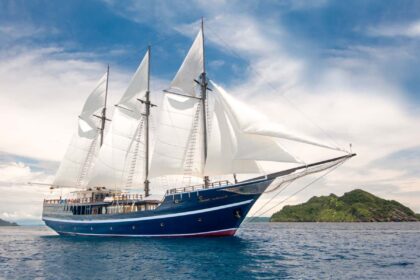 Dewi Nusantara liveaboard schooner under full sail near a small green island