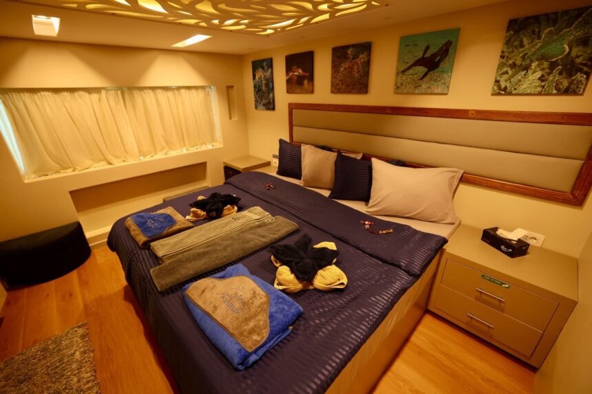 liveaboard cabin with a double bed, folded towels and marine art above the headboard