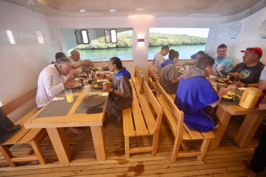 divers eating breakfast together at wooden tables with a shoreline view
