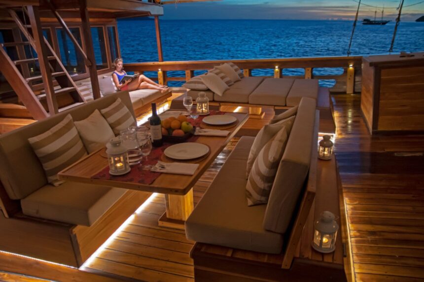 Guest reading on a lounge deck at sunset aboard the Coralia with a dinner table set nearby