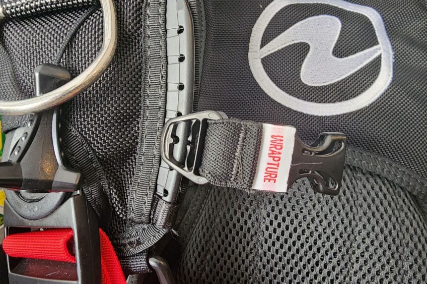 Close-up of the Aqualung Axiom i3+ chest strap buckle and Wrapture harness label beside a stainless D-ring