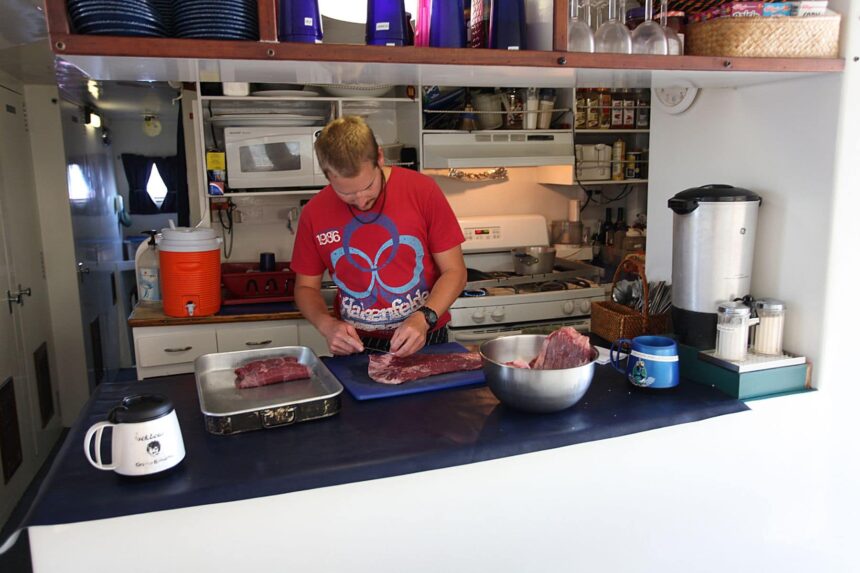 Crew member preparing meat in the galley kitchen