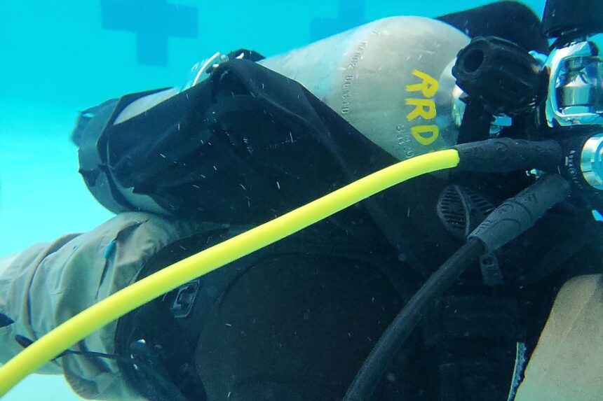 Close-up of the Aqualung Rogue underwater in a pool with the yellow inflator hose over the shoulder