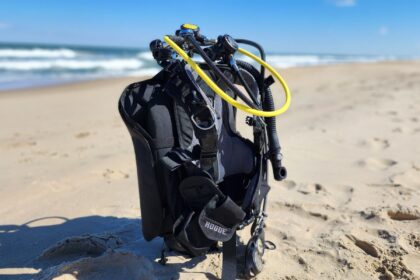 Aqualung Rogue BCD rigged with a regulator and yellow inflator hose standing on the beach before a test dive