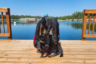 Hollis STS back inflation BCD in black and red standing on a lake dock during DIVEIN testing