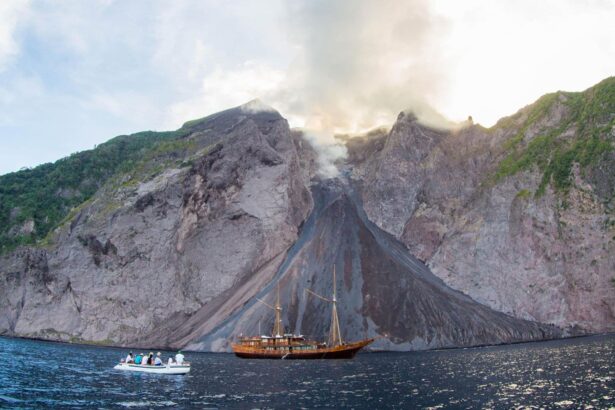 Damai II liveaboard anchored near a smoking volcanic slope in Indonesia, with a tender ferrying passengers nearby