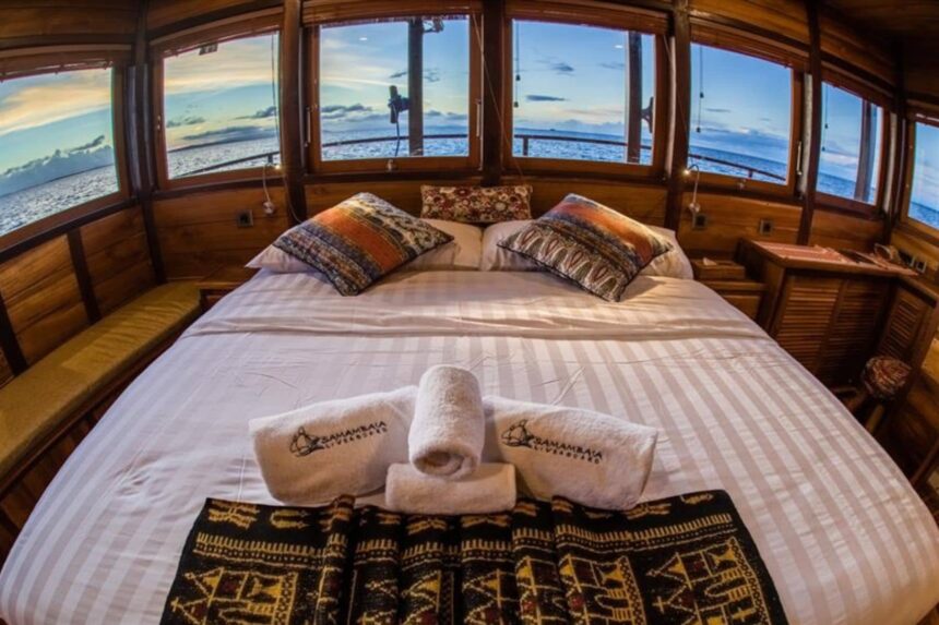 Wide bed with patterned pillows and ocean view windows aboard the Samambaia