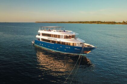 Emperor Virgo liveaboard yacht anchored off a palm-lined shore at sunset
