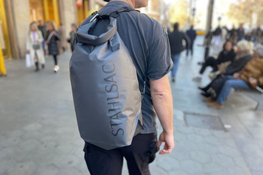 Stahlsac Dry Bag Worn On Back Man carrying a gray Stahlsac dry bag as a backpack while walking down a city street