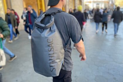Man carrying a grey Stahlsac Drylite roll-top dry bag as a backpack along a busy city street