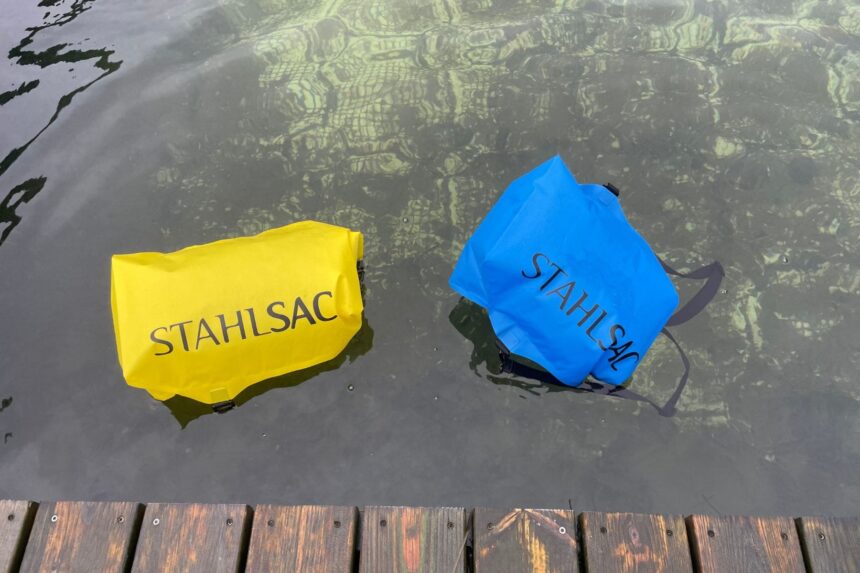 Yellow and blue Stahlsac Drylite dry bags sealed and floating on the water next to a dock