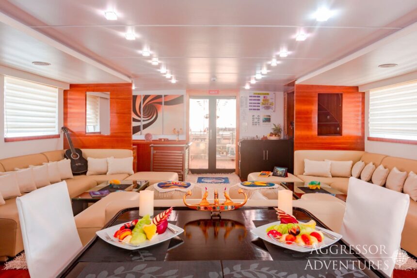 Spacious lounge with white sofas, a guitar, and a dining table aboard the Red Sea Aggressor II
