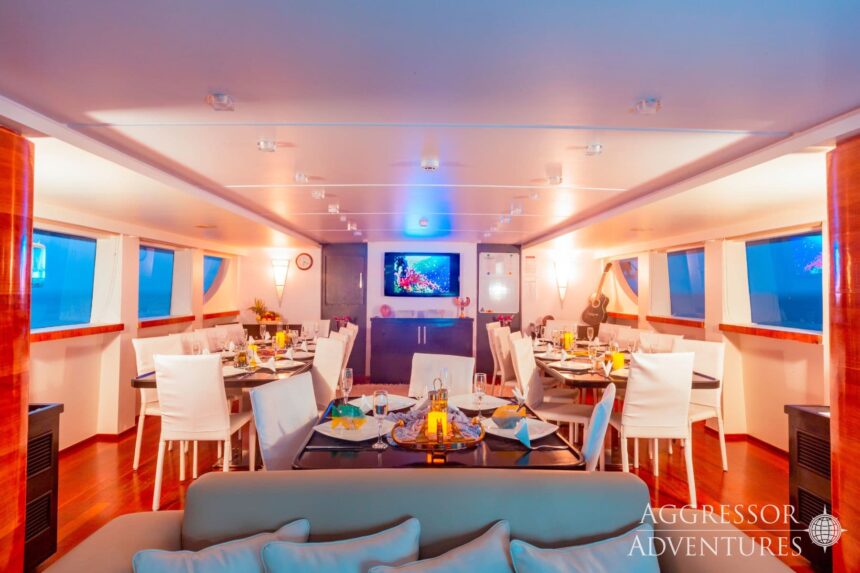 Dining tables set for dinner in the illuminated interior of the Red Sea Aggressor II