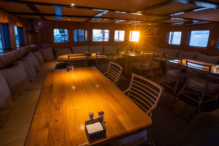 Indoor lounge and dining tables aboard the Pindito liveaboard at dusk