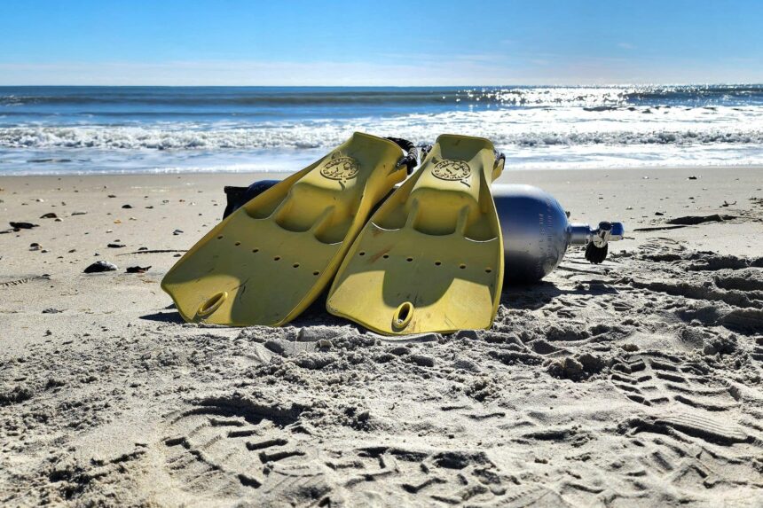 Yellow ScubaPro Jet Fins leaning on a dive cylinder on a wide sandy beach under blue sky