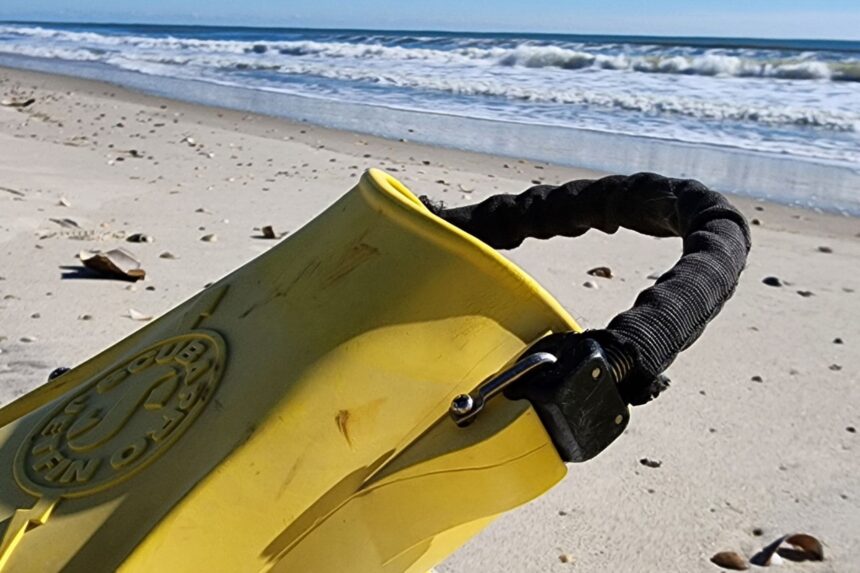 Nylon-covered spring strap on a yellow ScubaPro Jet Fin propped on the sand with surf behind