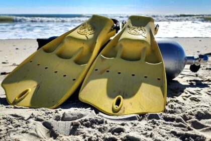 Pair of yellow ScubaPro Jet Fins propped in the sand beside a dive tank on a surf beach