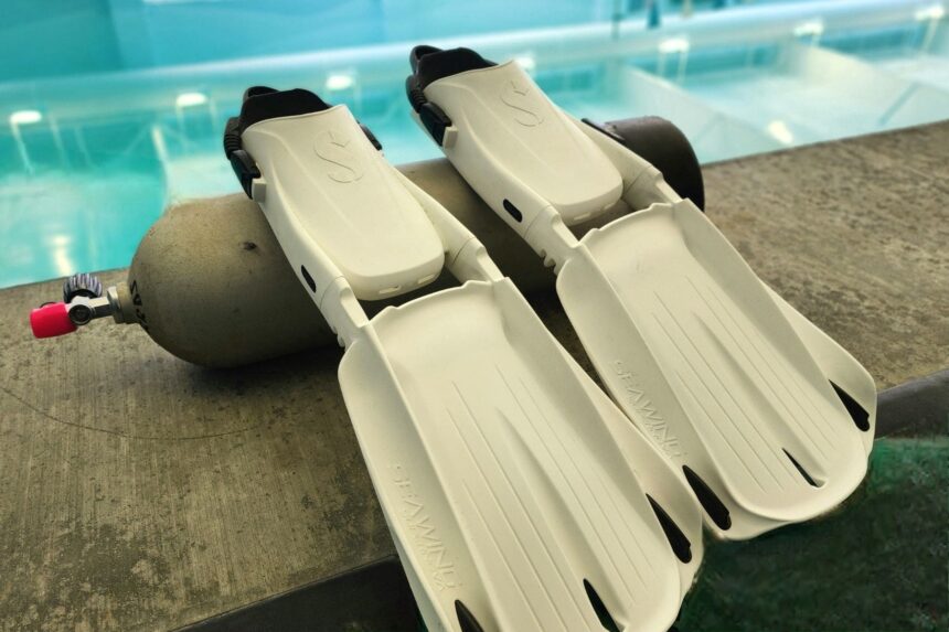 Pair of white ScubaPro Seawing Supernova fins on a pool deck beside a scuba cylinder