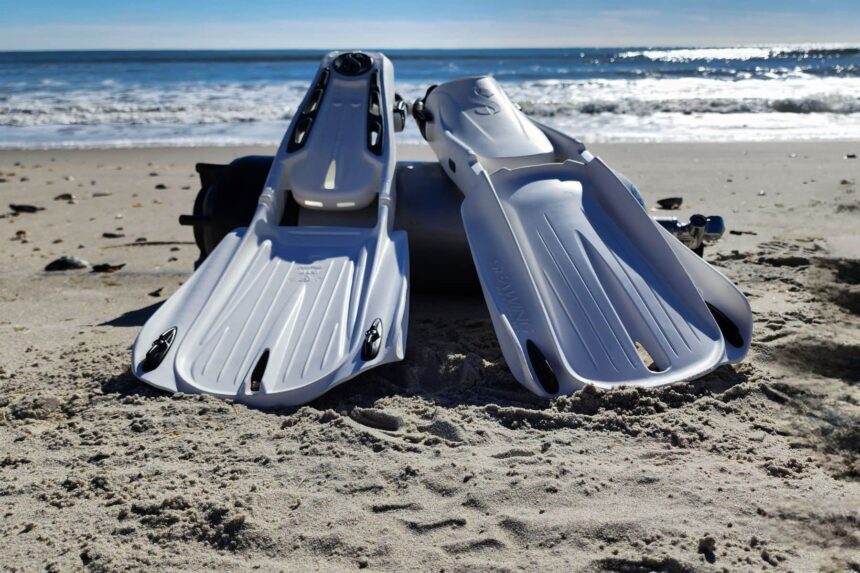 Pair of white ScubaPro Seawing Supernova fins standing in beach sand beside a dive cylinder