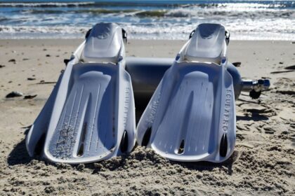 Pair of white ScubaPro Seawing Supernova fins standing in the sand next to a dive cylinder at the shoreline