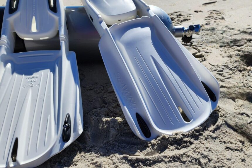 Close-up of two white Seawing Supernova blades resting in the sand with a cylinder behind