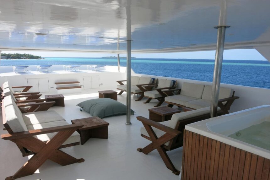 Shaded lounge deck with sofas, wooden chairs and a hot tub aboard the Blue Voyager liveaboard