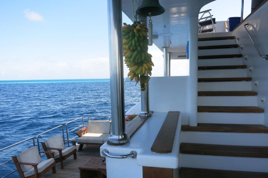 Wooden stairway to the upper deck with bananas hanging beside the ship's bell on the Blue Voyager
