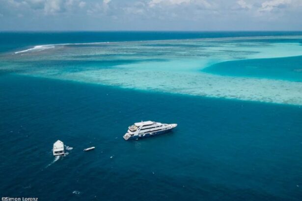 Aerial view of a liveaboard dive boat anchored beside a turquoise Maldives reef