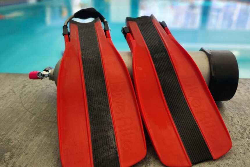 Pair of red Dive Rite XT fins propped against a cylinder at the poolside test session