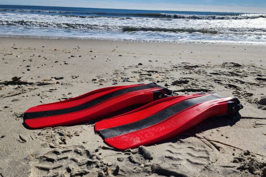 Red Dive Rite XT fins lying on wet beach sand with surf breaking behind them