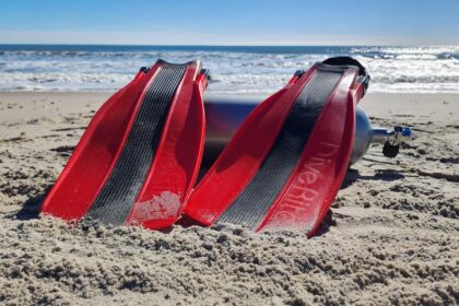 Dive Rite XT fins in red and black propped against a scuba cylinder on the beach during testing