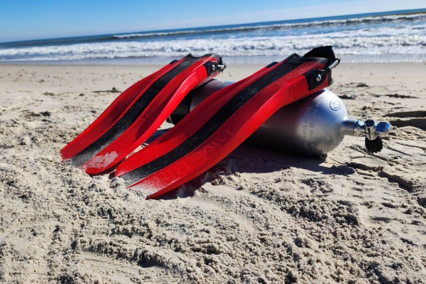 Red Dive Rite XT fins leaning against a scuba cylinder on the beach before a test dive