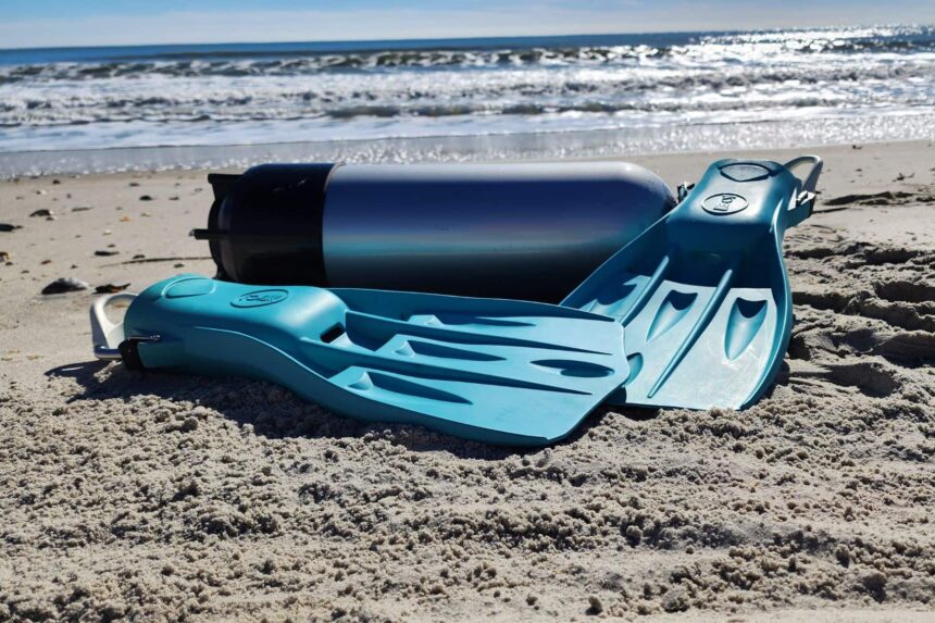 Fourth Element Tech fins resting in the sand next to a scuba cylinder at the beach test site