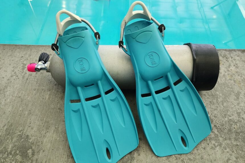 Fourth Element Tech fins in aqua leaning on an aluminum cylinder at the edge of the pool